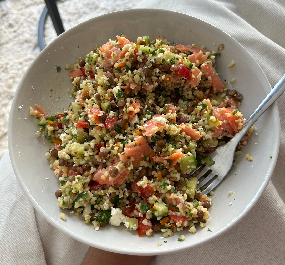 Bulgur lentil salad with hummus dressing, cucumber, tomato and fresh herbs in a bowl, with trout smoked ribbons