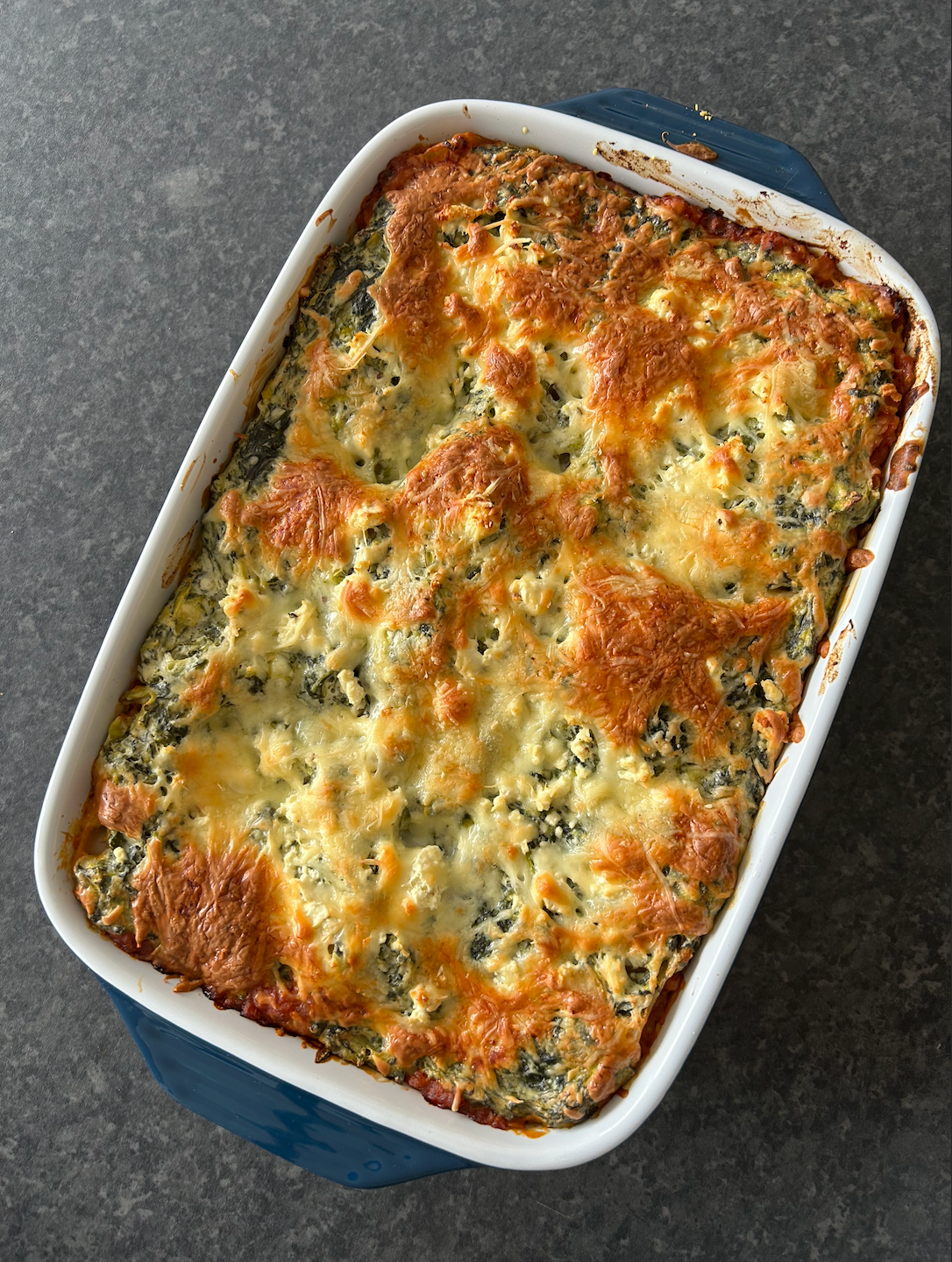 Golden baked spinach, cottage cheese and red lentil lasagna in a baking dish with visible layers of tomato lentil sauce, creamy spinach filling and melted mozzarella on top.