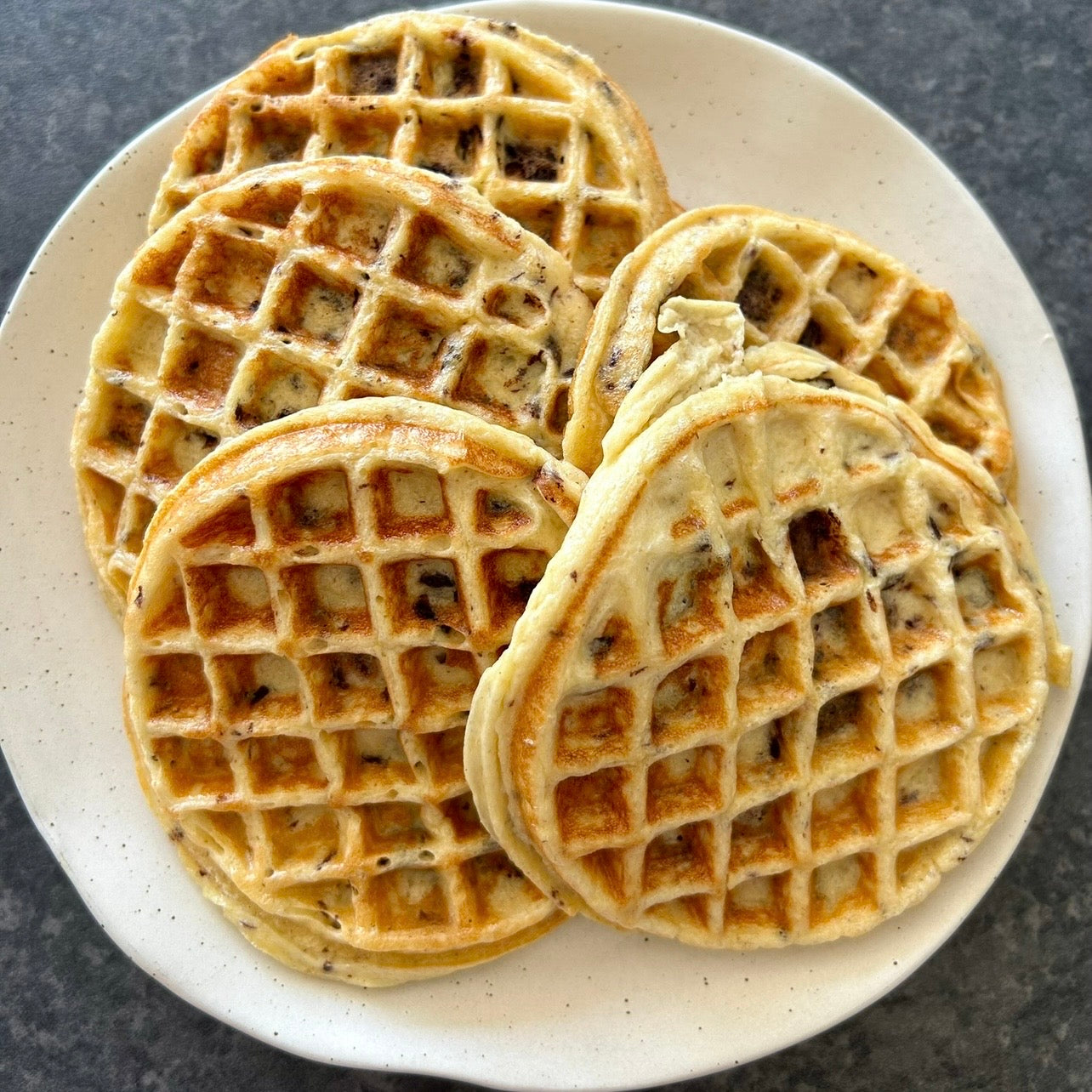 Golden cottage cheese protein waffles with chocolate chips stacked on a plate.