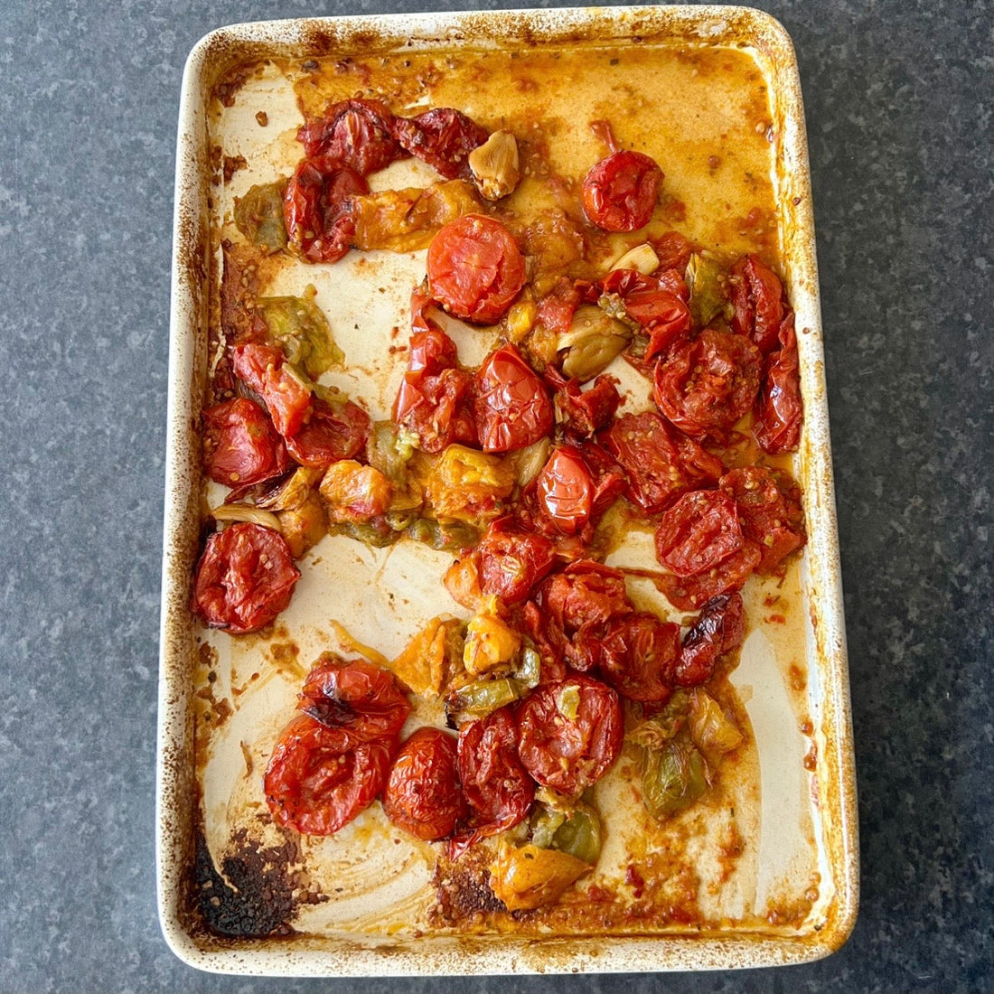 Tray of slow-roasted tomatoes with garlic and herbs, soft and caramelised.
