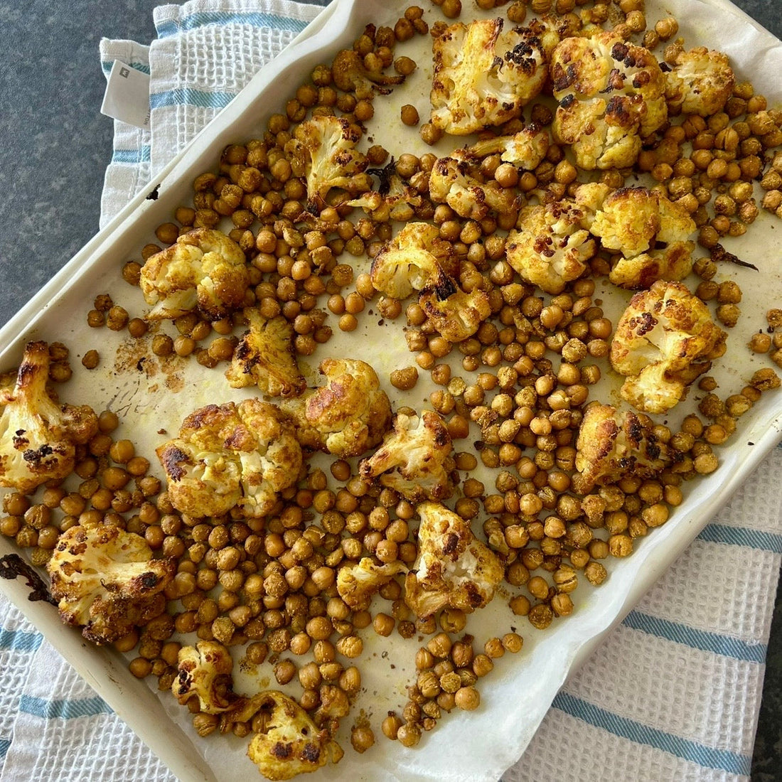 Roasted cauliflower and chickpeas with spices and crispy caramelised edges on a baking tray.