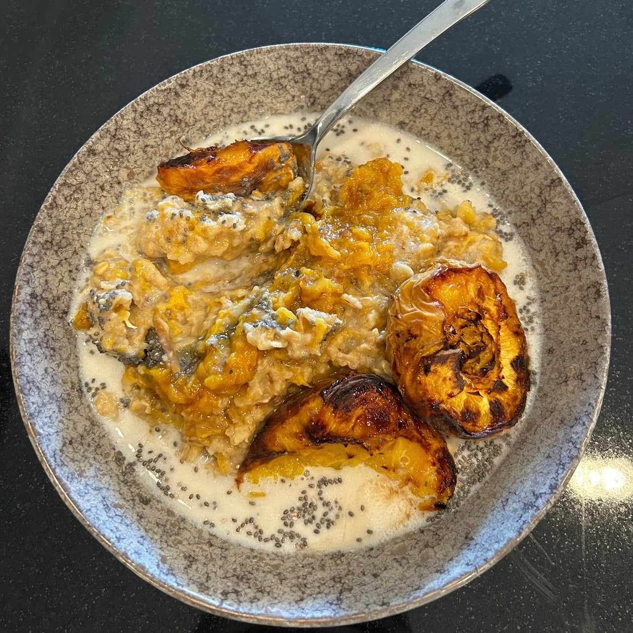 Creamy peach oatmeal topped with roasted peaches and maple syrup.